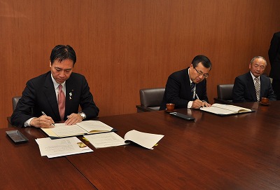 写真：仮契約書にサインする青木社長と阿部知事